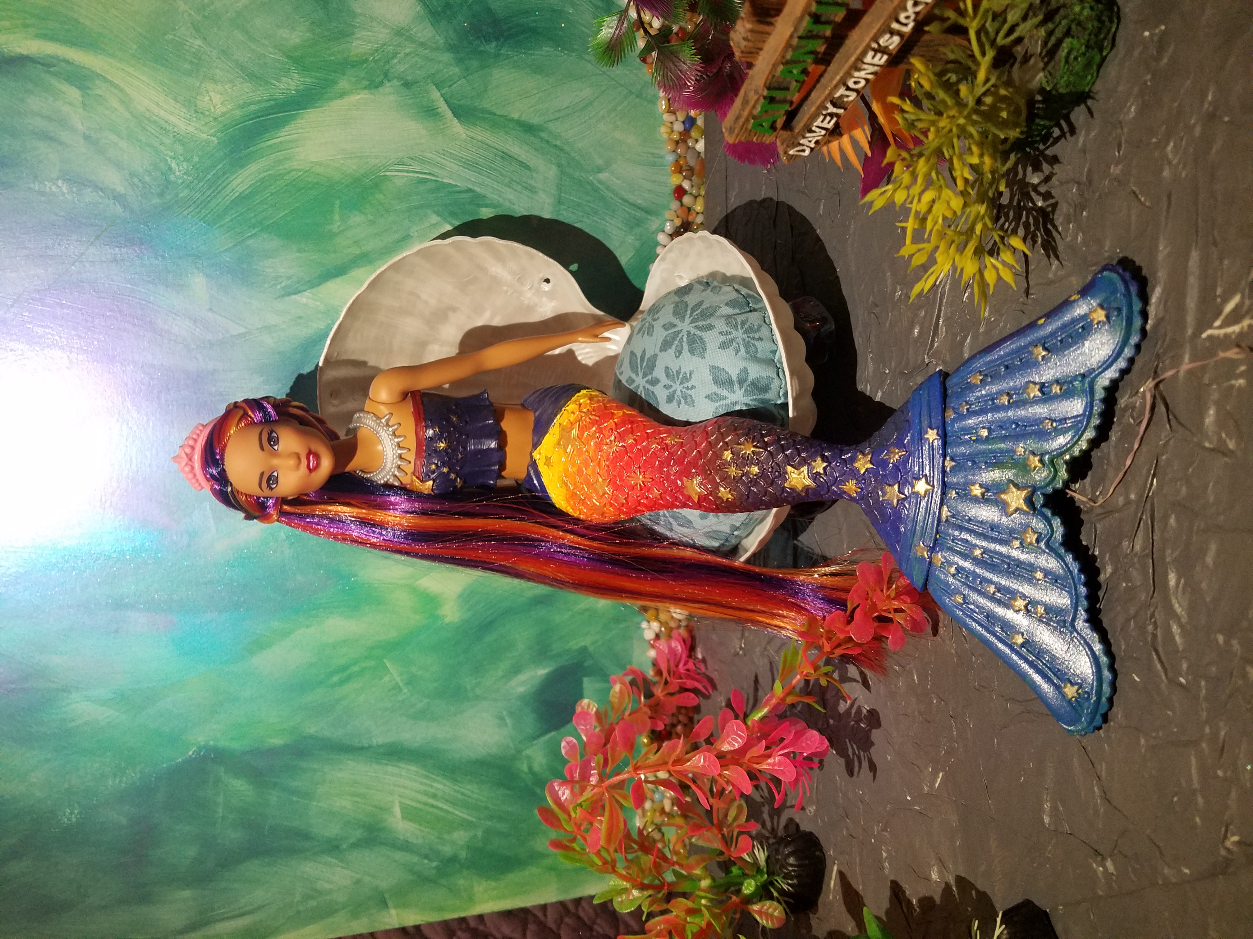 Dreamtopia mermaid Barbie with medium skin tone, her tail painted in the colors of the sunset, her tail flipper is blue gradiated to yellow. He hair is long and rooted to match her tail in color.