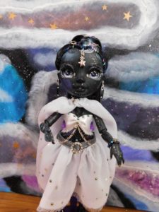 Photos of Shadow High doll Shanelle Onyx (with almost jet black skin and black hair, purple, blue and teal streaks), her skin is dotted with colored cloud splotches and freckled with stars, giving her the illusion of wearing galaxies.